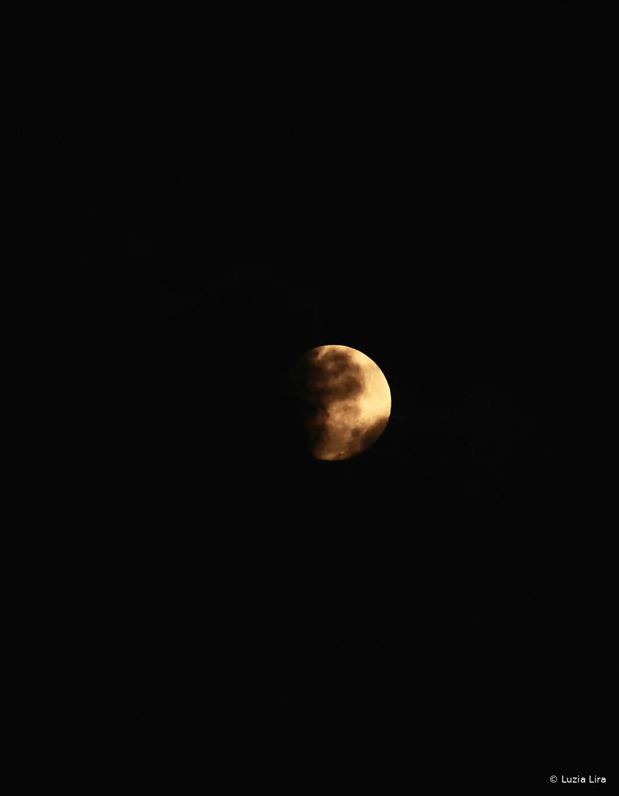 Lua em tons dourados parcialmente coberta por nuvens no céu escuro